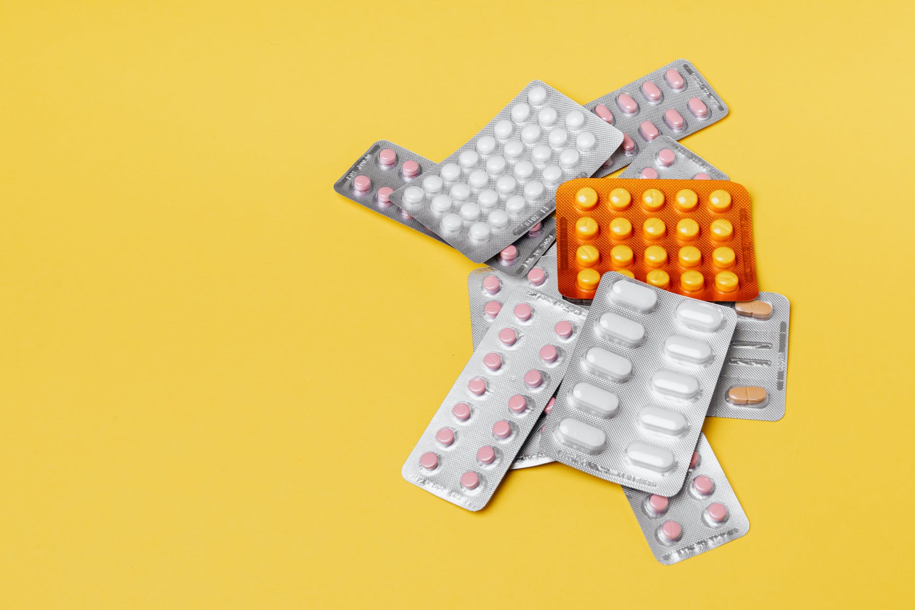 heap of various pills in blisters on yellow background