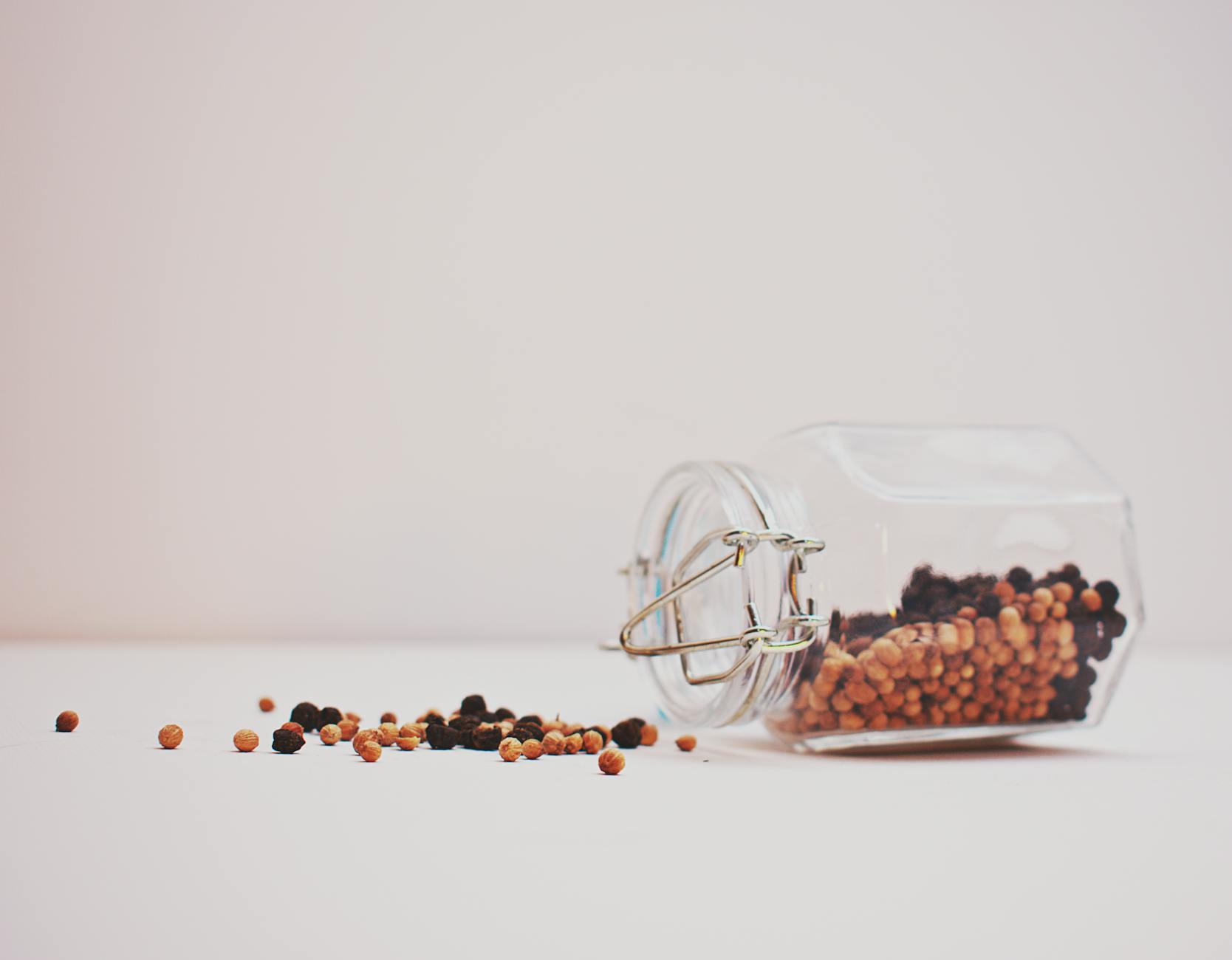 black and brown peppercorns spilling from glass jar